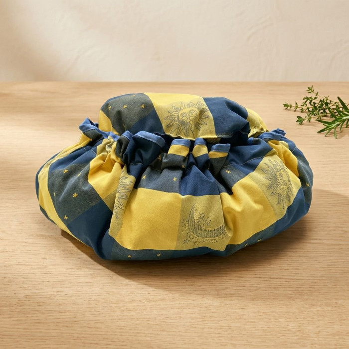 Sac poupé rond en tissu jaune et bleu, motif soleil et étoiles, posé sur une table en bois. Produit Marmite norvégienne Oliver's