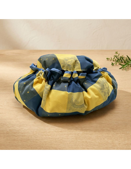 Sac poupé rond en tissu jaune et bleu, motif soleil et étoiles, posé sur une table en bois. Produit Marmite norvégienne Oliver's